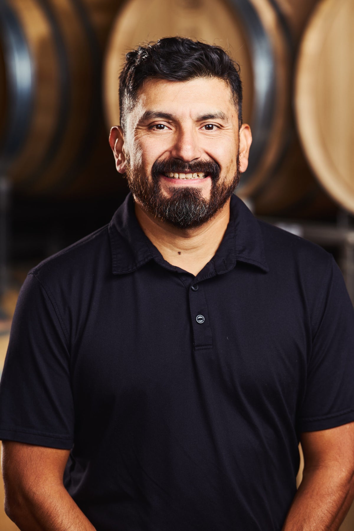 Miguel Lopez Associate Vineyard Manager headshot in front of wine barrels