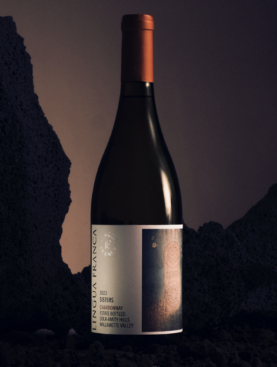 A bottle of 2023 Sisters Chardonnay against dark rock